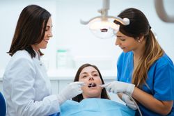 Dentist and assistant examining mouth of patient in chair with tools