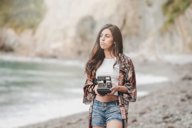 Woman with camera on shore near stones and water