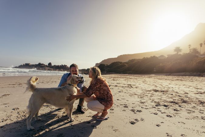 Mature man and woman petting their dog on the shore