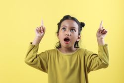 Positive Asian Little Girl Points Above Show Place for Advertising Text Surprised