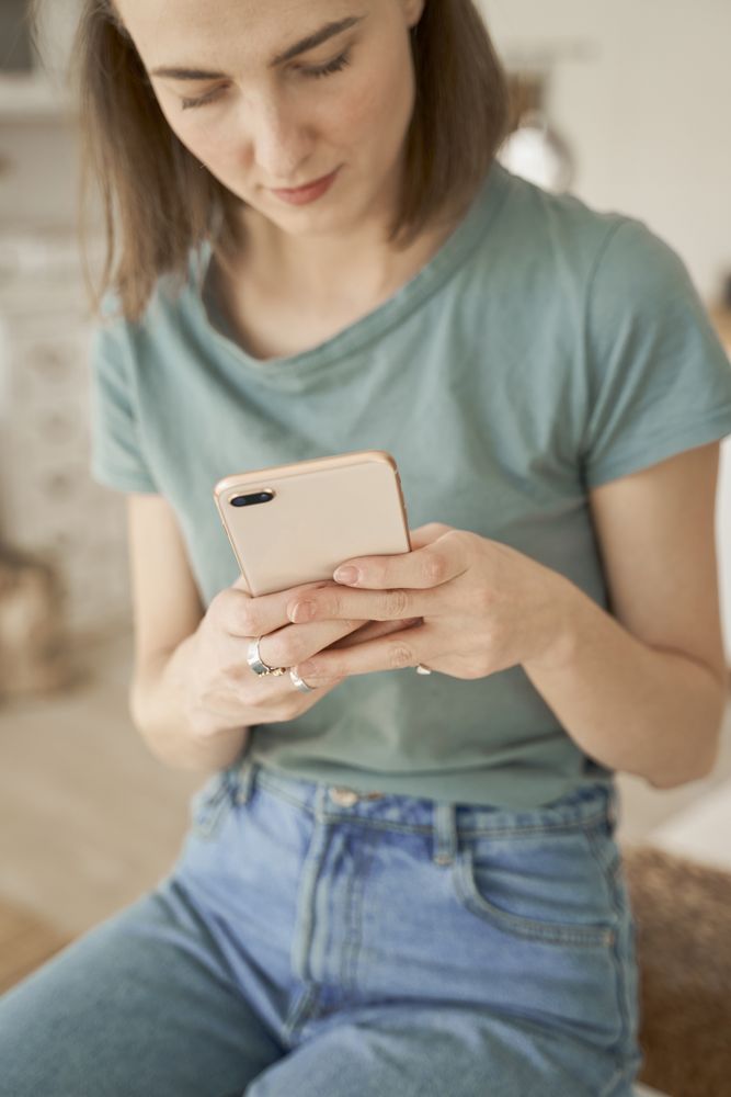 Relaxed women sitting on washing machine and browsing smartphone
