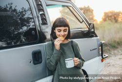 Woman with dark hair eating a cookie with coffee next to a van 5RDZ1b
