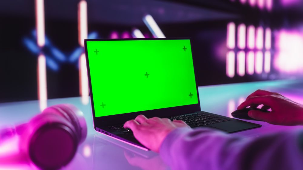 Over the Shoulder Footage with an Anonymous Gamer Playing an Online Video Game on a Laptop Computer with Mock Up Green Screen Display. Person Sitting in a Room with Futuristic Neon Design