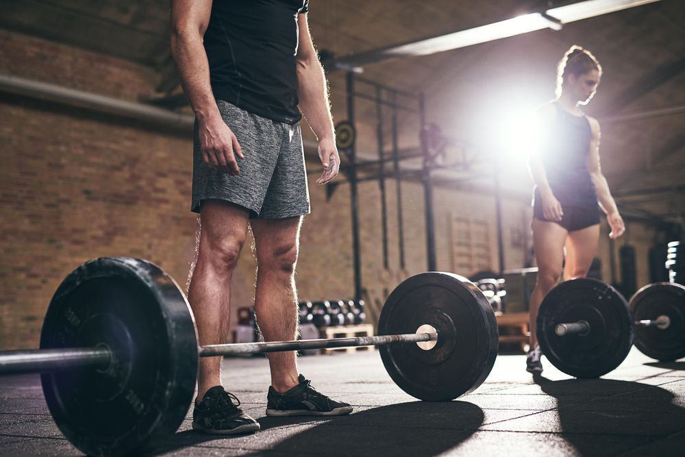 Crop shot of male standing beside barbell with weights