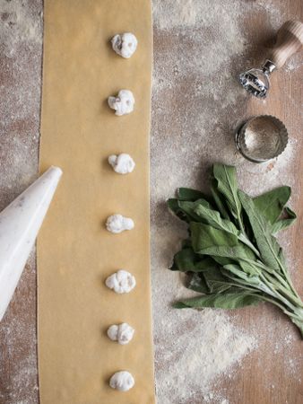 Crop hands squeezing stuffing on ravioli dough near sorrel