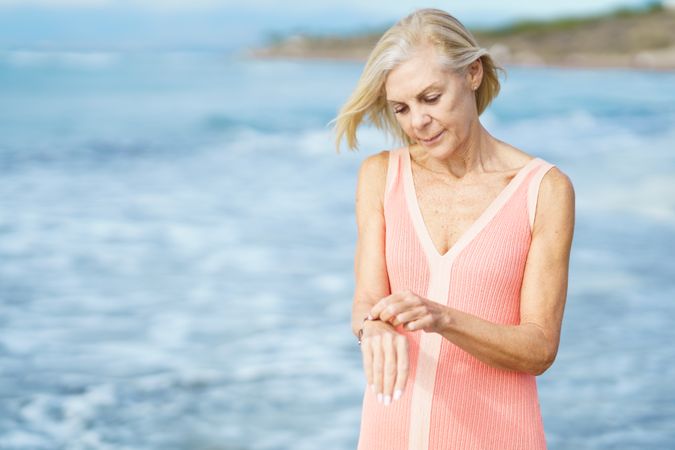 Older woman looking down at her wrist while walking along coast