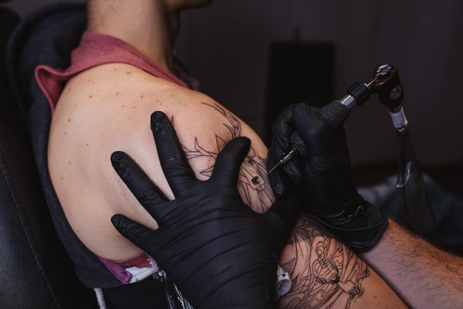 Master doing tattoo on forearm of male customer