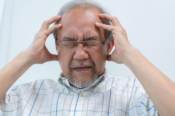 Older male with his hands holding his head in pain
