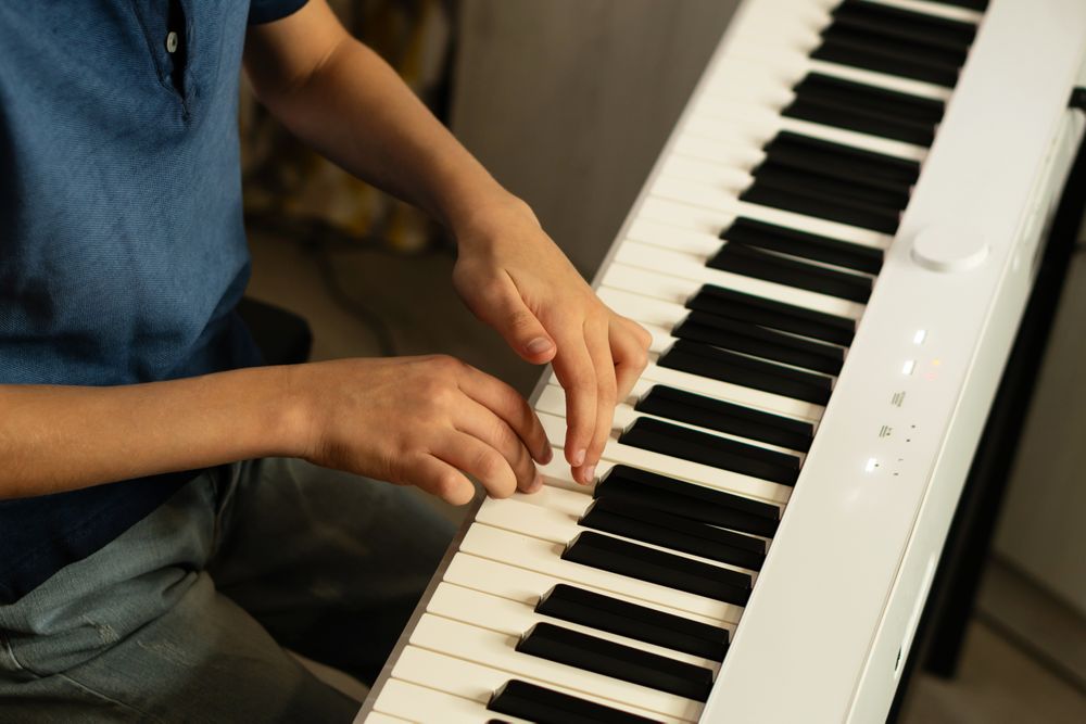 Close-up boy’s hands playing white piano keyboard