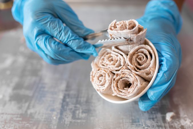 A worker is putting chocolate ice cream rolls in a tub using tongs and latex gloves