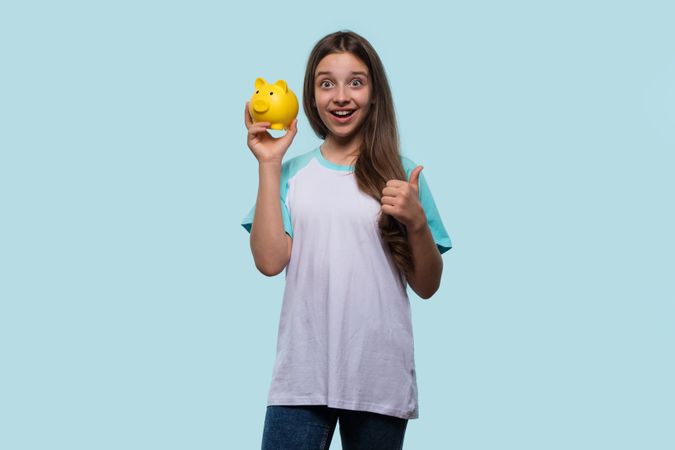 Girl excitedly holds yellow piggy bank and gives thumbs up