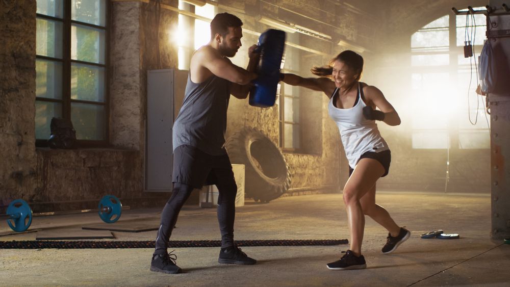 Athletic Woman Hits Punching Bag that Her Partner  Trainer Holds.