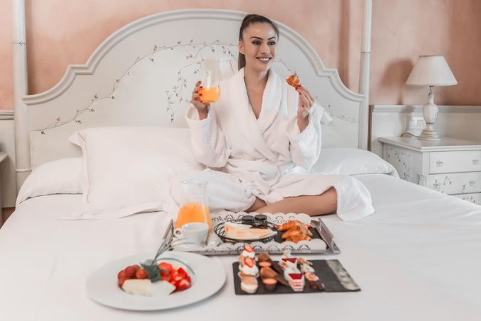 Woman in bathrobe eating breakfast on bed in hotel room