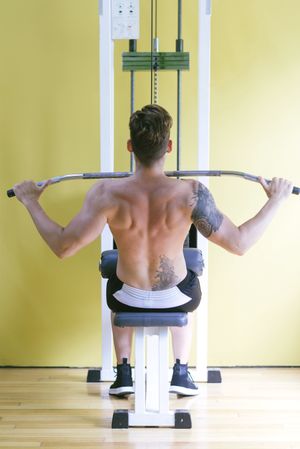 Back of tattooed male pulling down bar to his chest on weight machine