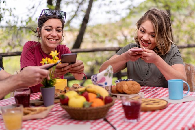 Two women taking picture of their brunch setup on smartphones