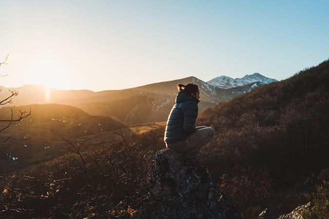 Female traveler sitting on mountain slope at sunset