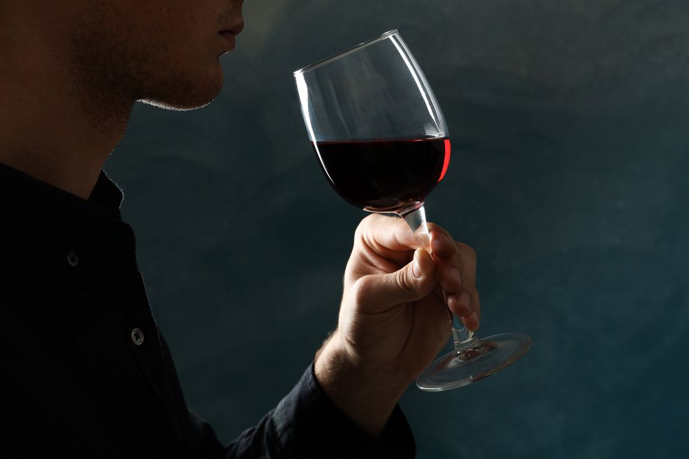 Young man holding red wine glass against dark background, space for text