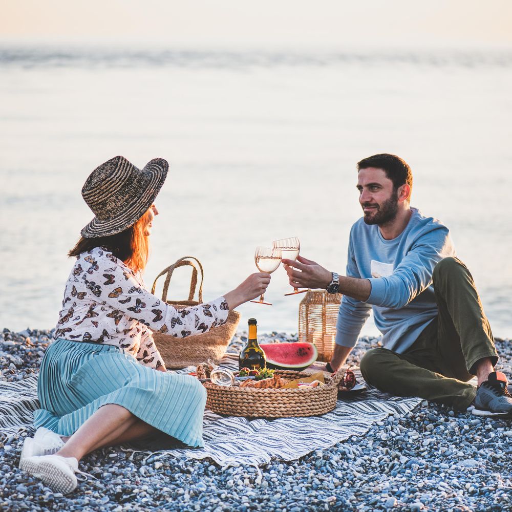 Couple toasting with wine glasses at summer picnic by the ocean, square crop
