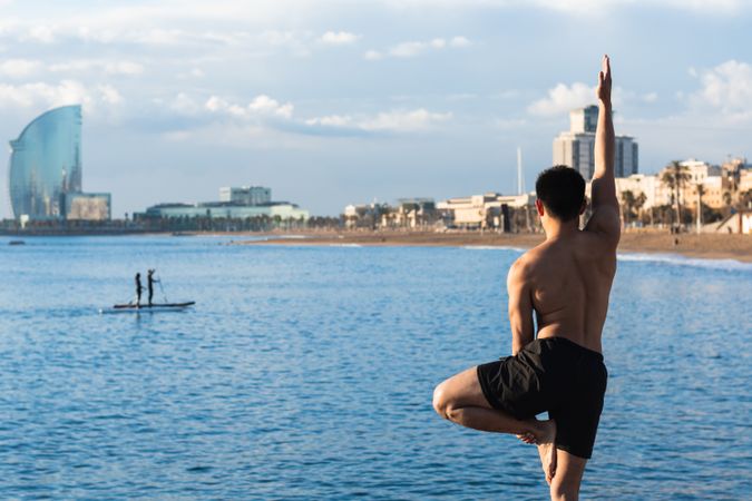 Shirtless man balancing in yoga pose on beach