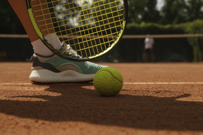 Woman leg, racket and tennis ball on clay court