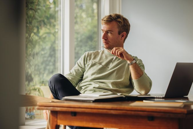 Man sitting at home holding eyeglasses looking away and thinking