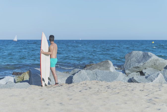 Back of male surfer standing on rock near ocean with board