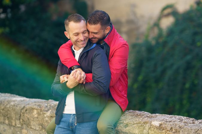 Cute male couple holding each other by the river, copy space with sun flare