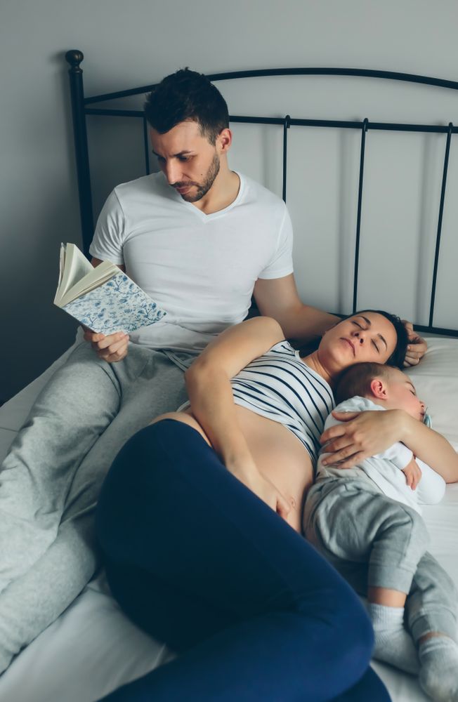 Man reading while his pregnant wife and son are sleeping