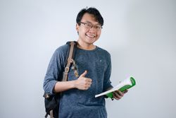 Asian young male student wearing bag and holding book smiling and happy expression
