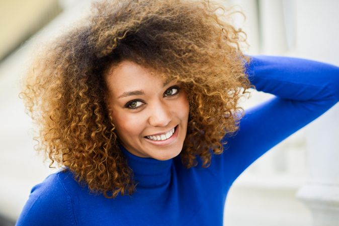 Female with curly hair smiling while wearing bright blue shirt outside
