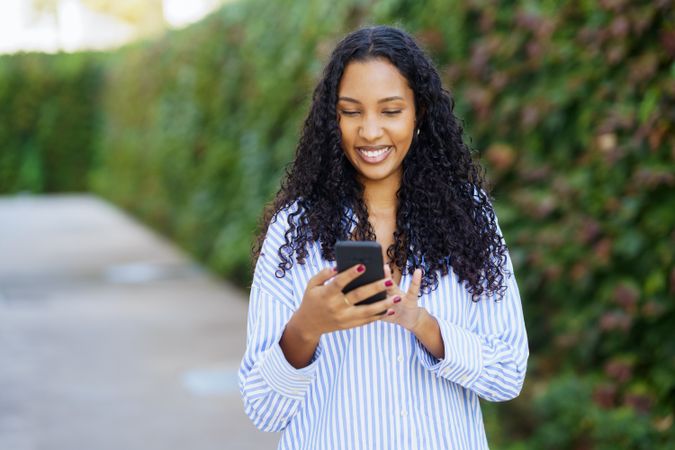 A cheerful woman uses her smartphone in a vibrant green space, enjoying summers joy