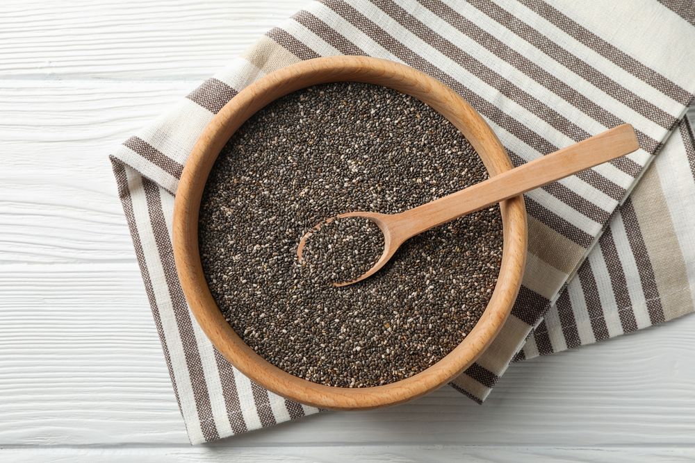 Wooden bowl with chia and spoon on wooden background, top view