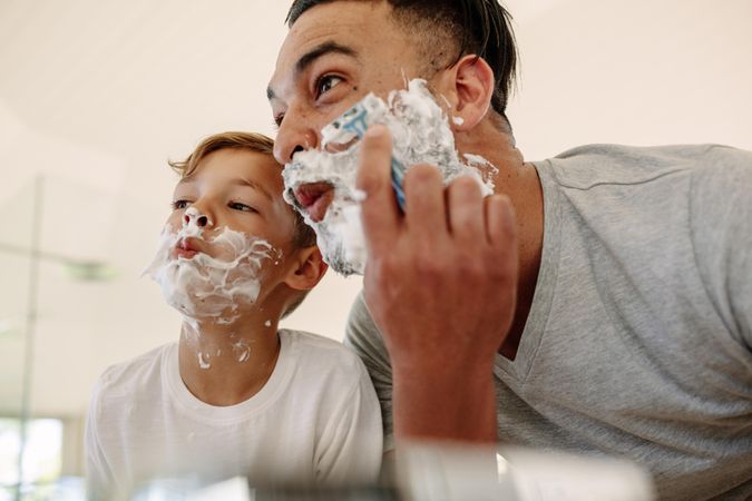 Father and son making funny faces while shaving in bathroom