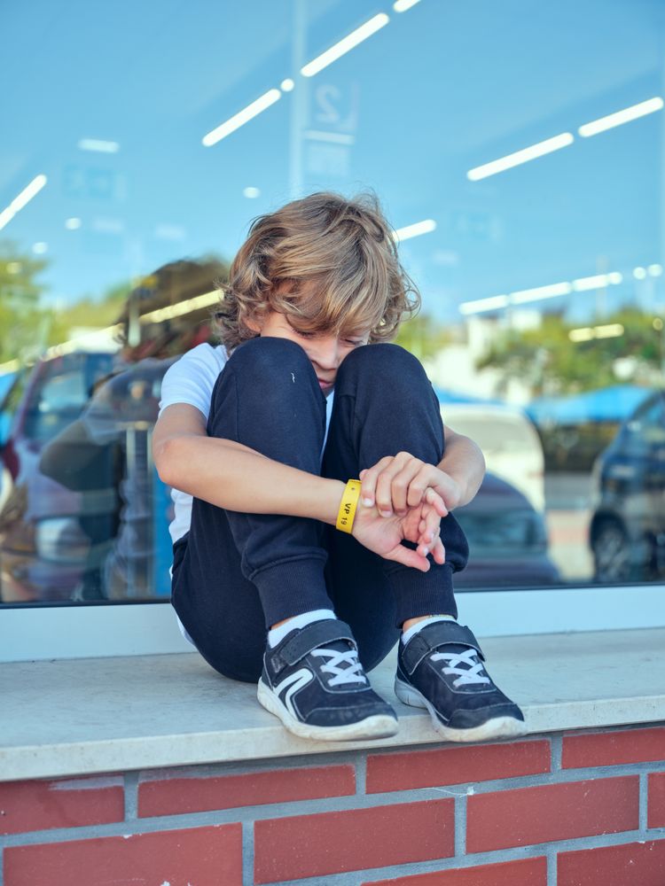 Sad boy sitting on windowsill in city