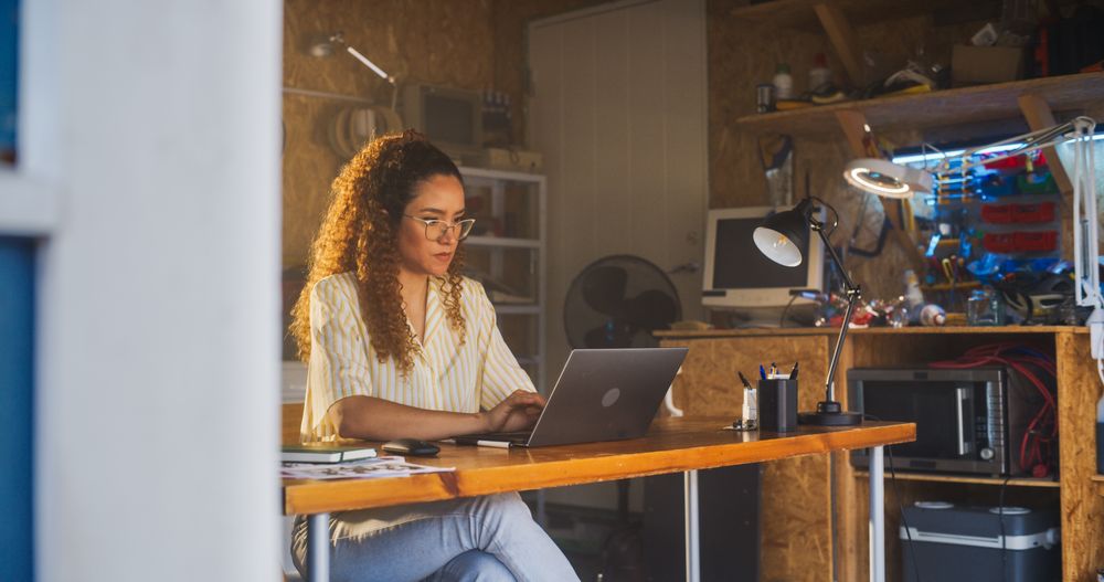 Hispanic Female Programmer Writing Code On Laptop Computer In Garage At Home.