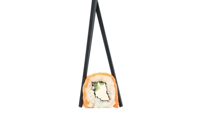 Chopsticks with sushi roll isolated on light background