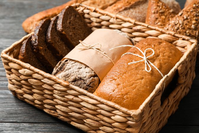 Bakery products in straw basket on wooden background, closeup and space for text