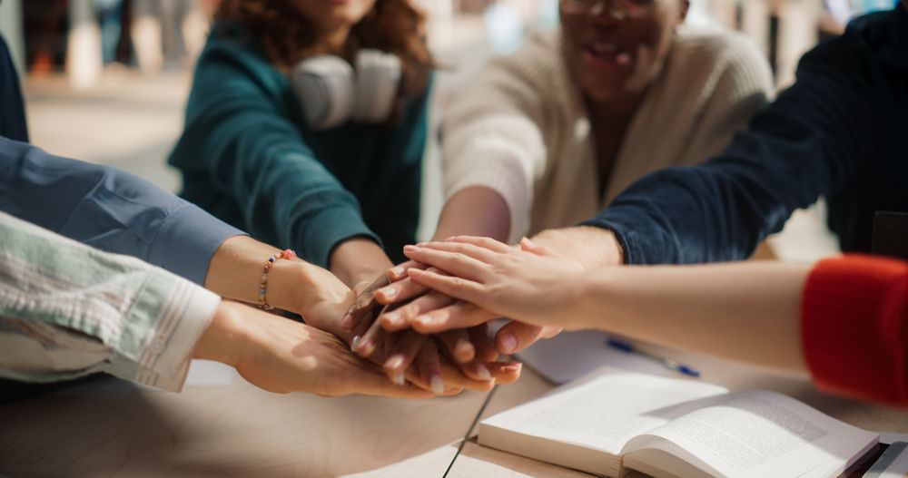 Diverse Group of Students Collaborating in a Library, Hands Joined in Unity.