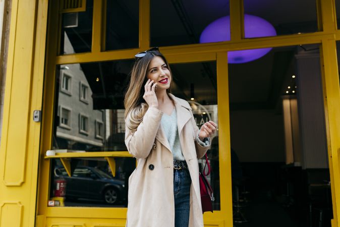 Young cheerful female standing near house with smartphone