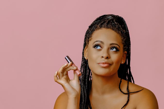 Black woman holding lip gloss while looking up