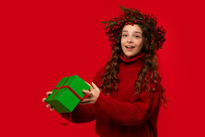 Teen girl in Christmas berry wreath holding green gift box.