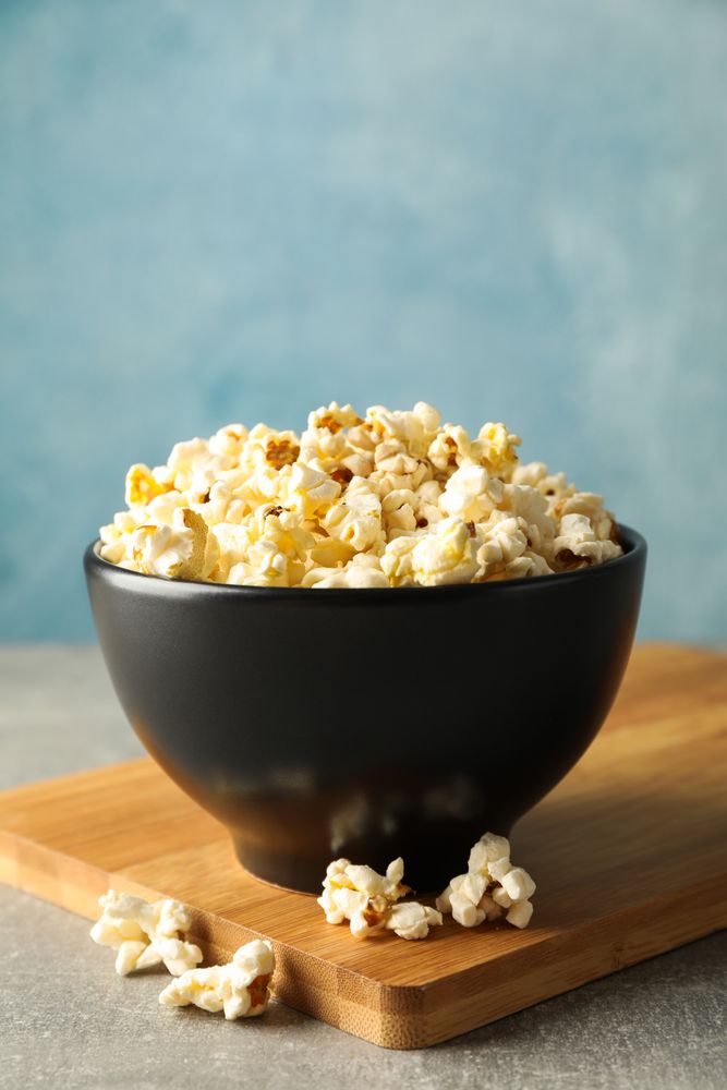 Bowl with popcorn and board on grey background, copy space