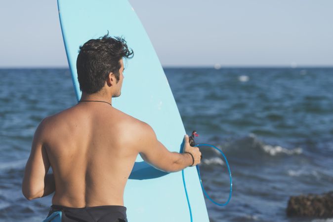 Male surfer holding blue board standing in front of the water