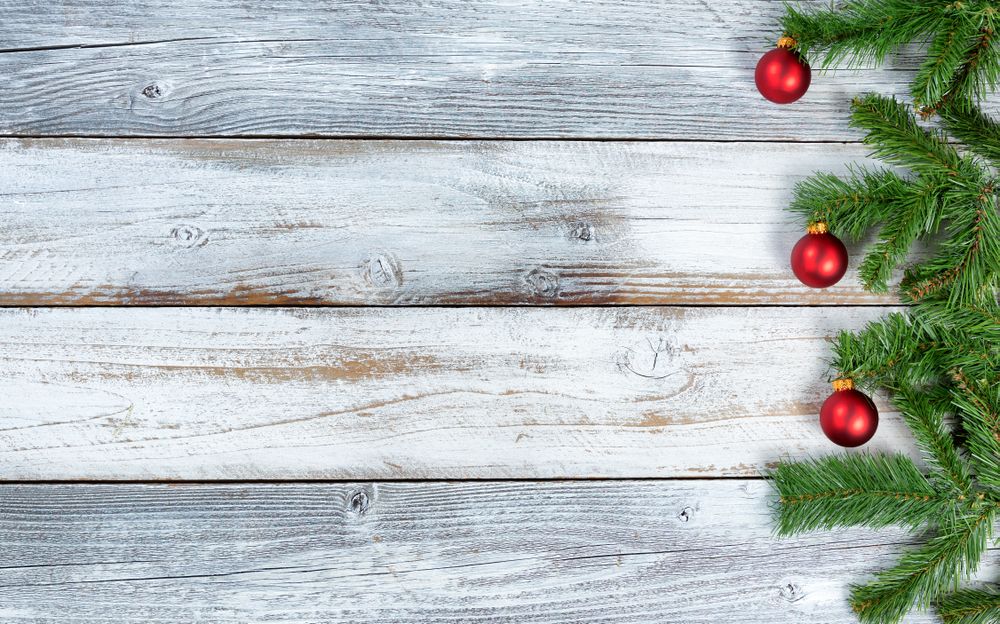 Christmas evergreen branches and red ornaments on rustic knotty wooden background