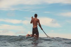 Man with paddle on surf board waving on water