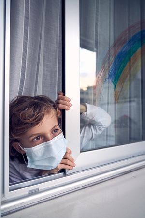 Boy in medical mask looking out window