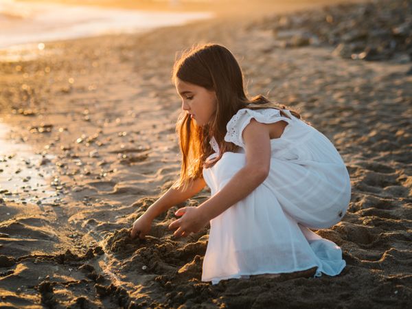 Adorable girl playing with sand on beach