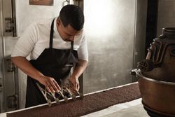 Man in apron working in professional kitchen cutting slices of cake