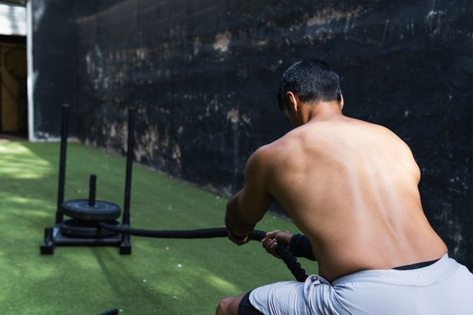 Anonymous muscular Hispanic sportsman pulling weight sled