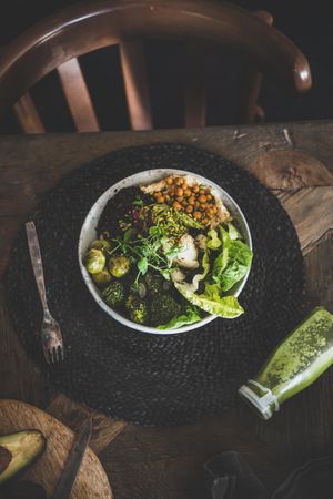 Healthy vegetarian bowl with smoothie, on table with dark chair, placemat, copy space